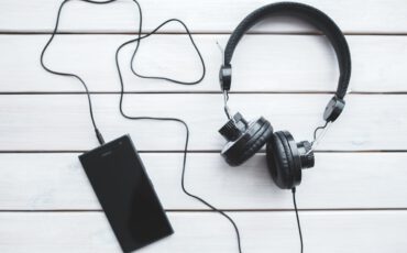 Een zwarte mobiele telefoon die is aangesloten aan een zwarte koptelefoon op een witte houte achtergrond